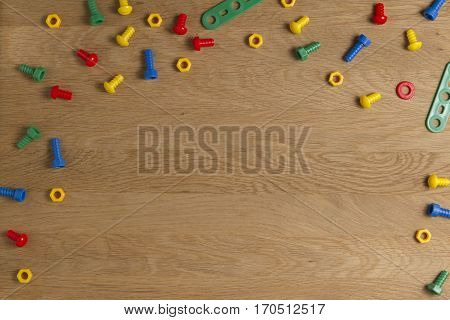 Kids construction toys tools: colorful screws and nuts on wooden background. Top view. Flat lay. Copy space for text