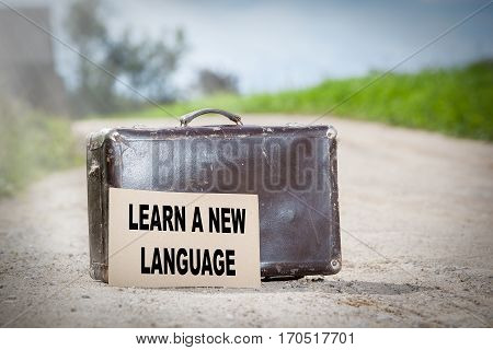 Learn a New Language. Old traveling suitcase on country road.