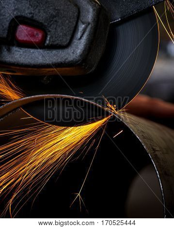Angle grinder cutting through pipe with orange sparks