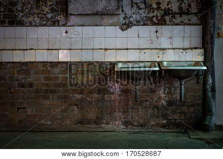 Two industrial sinks on tiled brick wall in abandoned warehouse