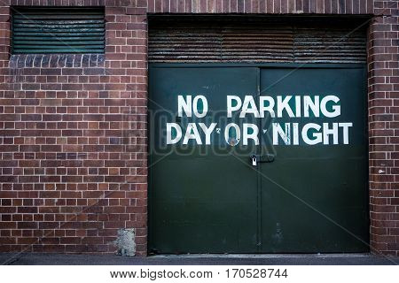 No parking day or night sign painted on green doors of brick building
