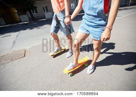 summer, relations, extreme sport and people concept - happy teenage couple riding short modern cruiser skateboards on city street