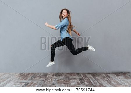 Full length image of Funny Woman jumping with open mouth in studio and looking at camera. Isolated gray background