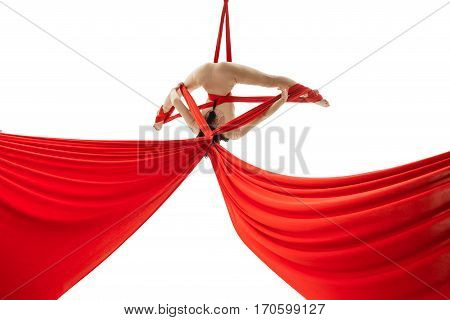 Pretty woman - aerial acrobat doing acrobatic tricks on red silks.  Young flexible aerialist performing on white isolated studio background