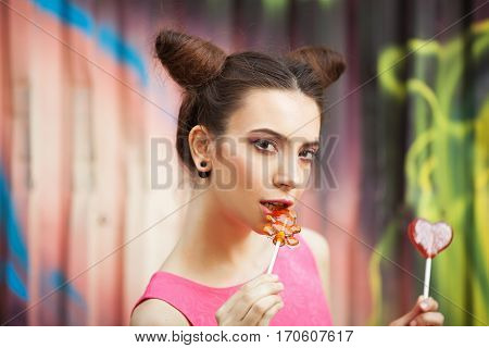Young girl in a pink dress with candy on a decorated background of graffiti wall