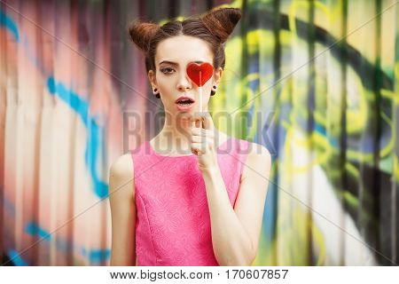 Young girl in a pink dress with candy on a decorated background of graffiti wall