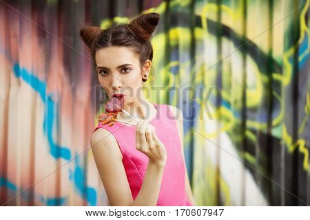 Young girl in a pink dress with candy on a decorated background of graffiti wall
