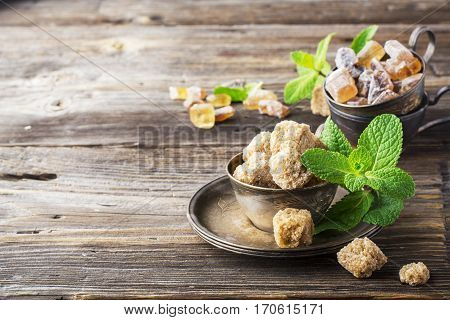 Lump brown cane sugar in a vintage metal dishes with a sprig of fresh mint on a simple wooden background. The concept of natural organic food. selective