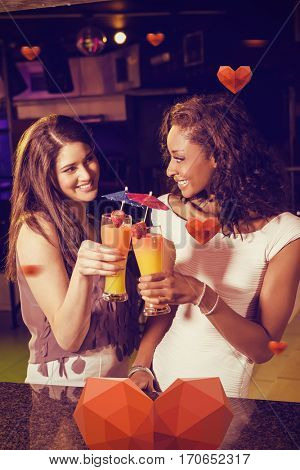 Female friends toasting cocktail glasses at bar counter against hearts