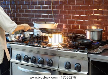 Chef is making flambe dish in restaurant kitchen, motion blur