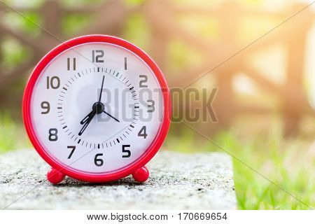 The red clock holding on the floor in the garden background.