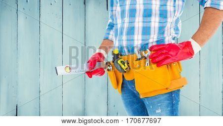 Mid section of handyman with tool belt and sprit level against wooden background