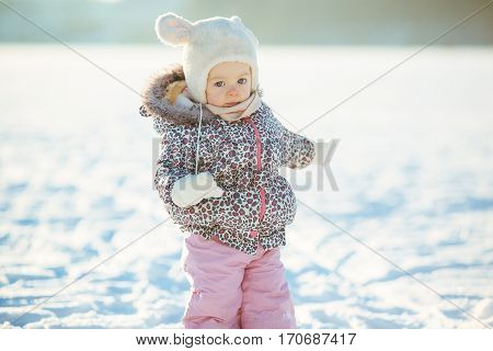 little girl walks through the snow in a warm jaket and hat