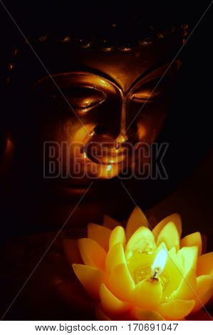 Buddha head in the dark, illuminated by a candle in the form of a lotus flower.