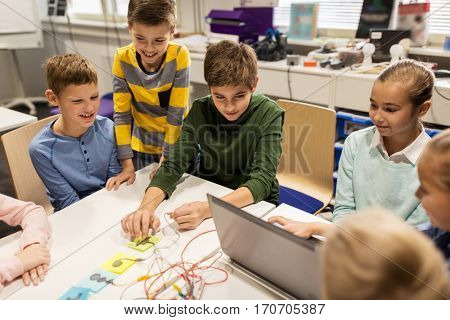 education, children, technology, science and people concept - group of happy kids with laptop computer playing with invention kit at robotics school lesson