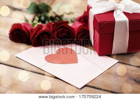 love, romance, valentines day and holidays concept - close up of gift box, red roses and greeting card with heart on wood (vintage effect)