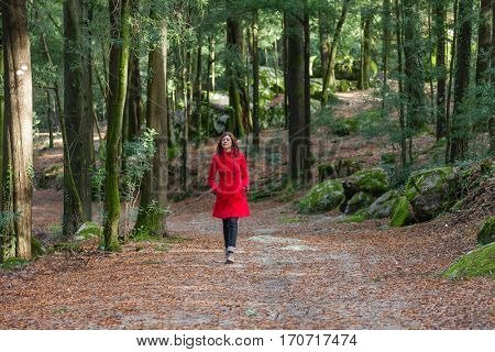 Young woman walking alone on a forest dirt path wearing a red overcoat on a cold winter day