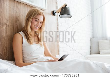 Smiling pretty woman lying on bed and using smartphone