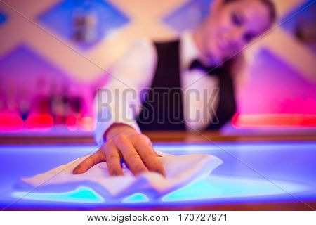 Barmaid cleaning illuminated bar counter with napkin
