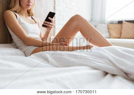 Cropped image of woman lying on bed with smartphone in bedroom