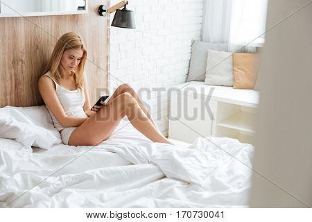 Young pretty woman lying on bed with smartphone in hands