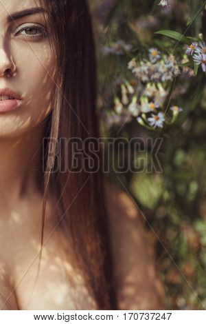 Beautiful young naked woman close-up portrait in flower meadow smiling and looking at camera. No clothes, naked tender girl in the blossoming bushes on spring. Half face framing