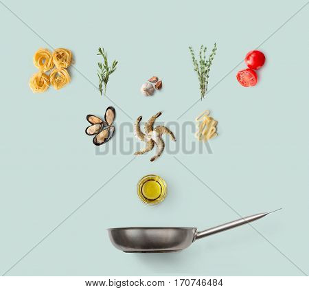 Cooking italian food, seafood pasta, isolated on blue. Frutti di mare with fettuccine spaghetti. Mussels, prawn, shrimp, calamari rings and other ingredients over frying pan
