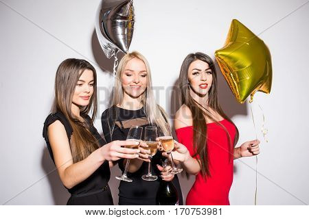 Cheerful young women drinking champagne talking and laughing with balloons on the party over white background