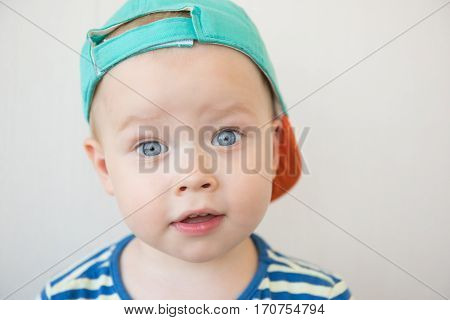 A cute white baby boy with big blue eyes is looking surprisingly into the camera. Portrait. Close-up