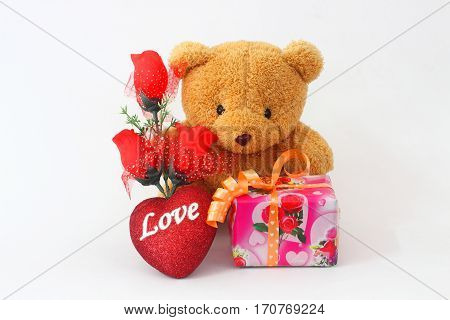 Brown teddy bear with a red rose and a gift box on a white background.