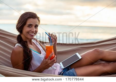 Portrait of woman holding mocktail while relaxing on a hammock on the beach