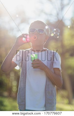 Cute young boy blowing bubbles through bubble wand in park