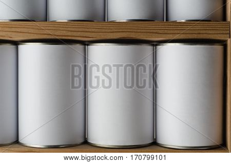 Rows of tin cans with unbranded blank white labels on wooden shelves.