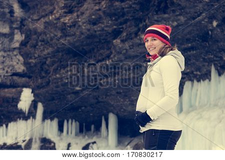 Young pregnant woman smiling on winter landscape. Icicles and snow in the background.