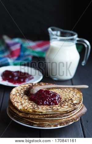 Homemade pancakes with raspberry jam on a dark wooden table. Top view with hands. Shrove Tuesday.