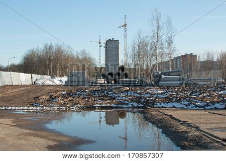 Belarus-March 20, 2016 Two cranes are on site construction site next to lay pipes and blocks for the construction of residential high-rise building, reflected in water, snow