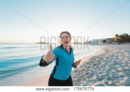 Smiling female runner show thumbs up. Summer day on the beach.