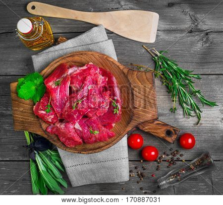 Pieces of fresh raw chopped beef meat on plate. Ingredients for chopped beef meat sage thyme basil rosemary tomatoes coriander pepper vegetable oil. Top view.