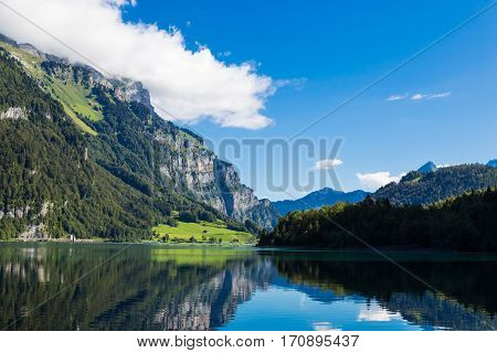 Mountain lake Klontalersee on background of majestic mountains reflected in the water and bright cloudy sky. Glarus Canton. Swiss Alps. Switzerland.