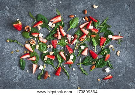 Ingredients for strawberry salad. Spinach leaves sliced strawberries nuts feta cheese on kitchen blackboard. Healthy food concept. Fat lay top view