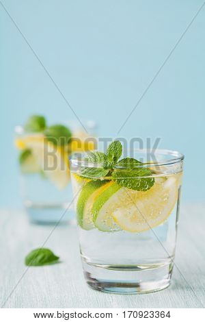 Mineral infused water with limes, lemons, ice and mint leaves on blue background. Homemade detox soda water recipe.