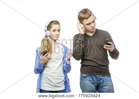 Beautiful teen age boy and girl in casual clothes standing on white background listening to music in headphones. School children. Isolated. Copy space.