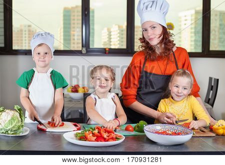 Three cute kids with mom making fruit salad in the kitchen. Healthy eating