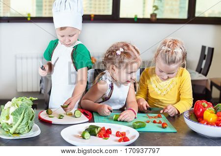 Three Cute Kids Are Preparing A Salad In The Kitchen