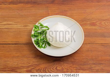 Piece of the fresh mozzarella cheese with twig of parsley on the saucer on an old wooden surface