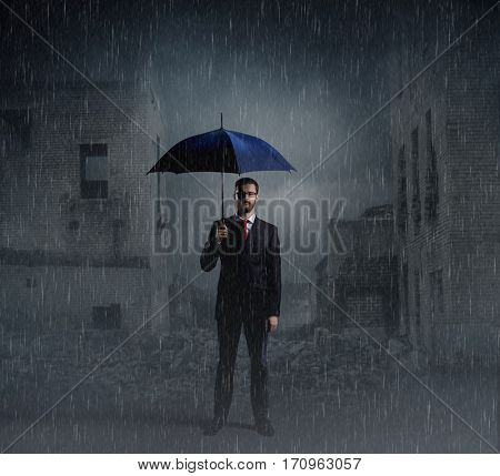 Businessman with umbrella standing over apocalyptic background. Crisis, default, setback concept.