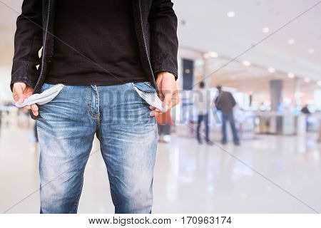 Man showing his empty pockets on blur shopping mall background.