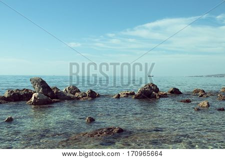 Serene seascape with rocks in the foreground and boat on horizon - Сyprus Paphos