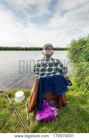 Unknown angler sitting on a chair for fishing in a small river. It's a cloudy in the Dutch summer season.