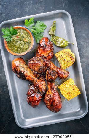 Traditional barbecue chicken drumsticks with corn and chimichurri sauce as top view in a silber fryer 